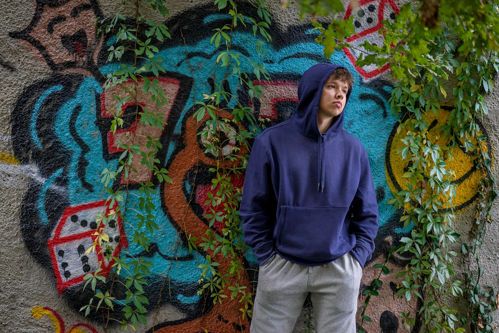Max Cooper III in a hooded sweatshirt in front of a vine-covered graffiti wall