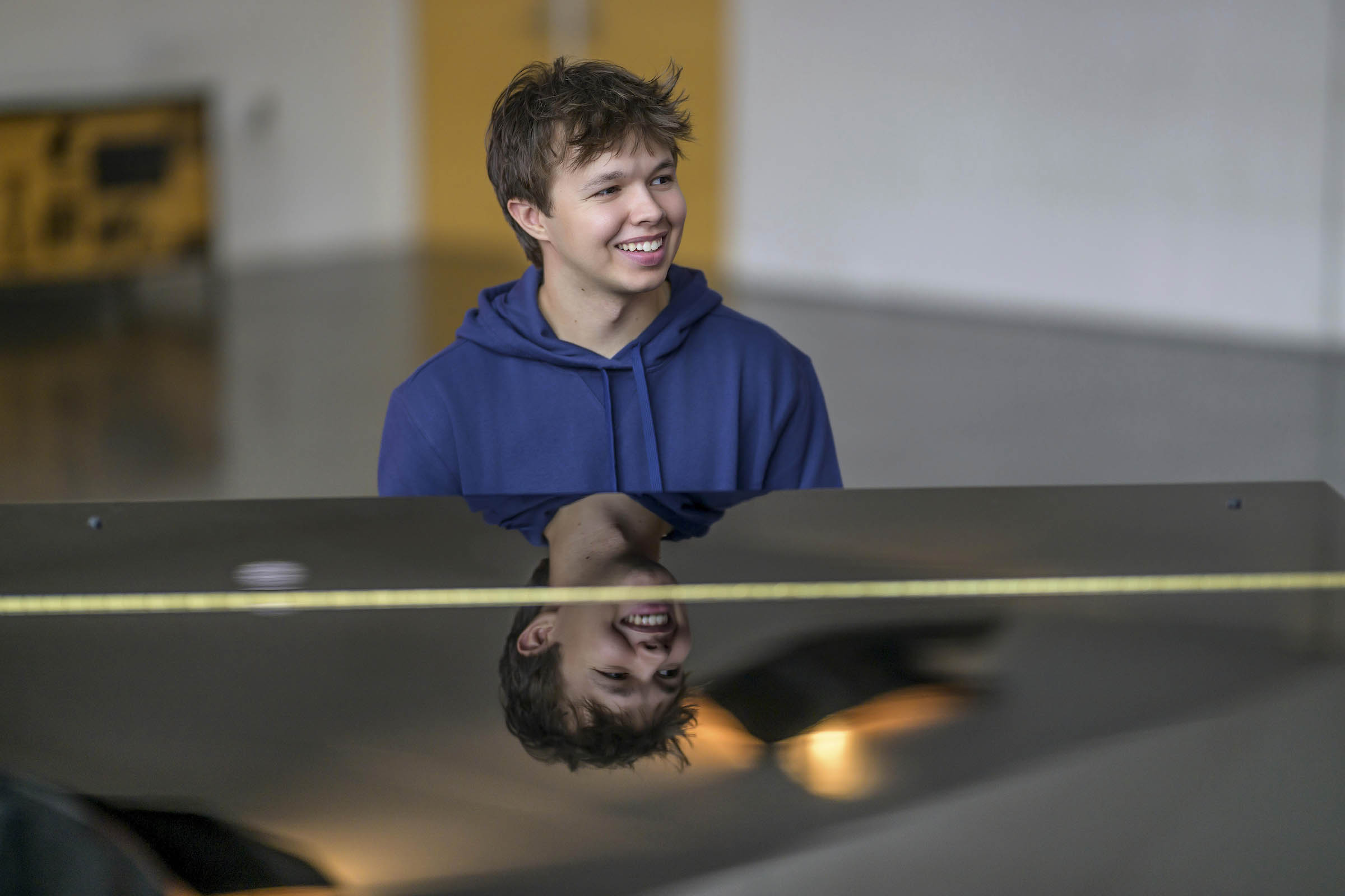 Max Cooper III smiling at a grand piano, reflected in its black lid